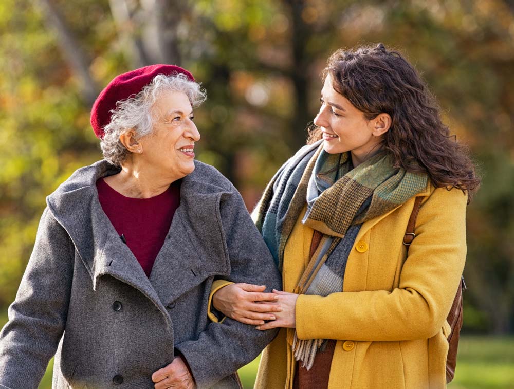 An elderly woman is assisted by a younger woman while out on a walk.