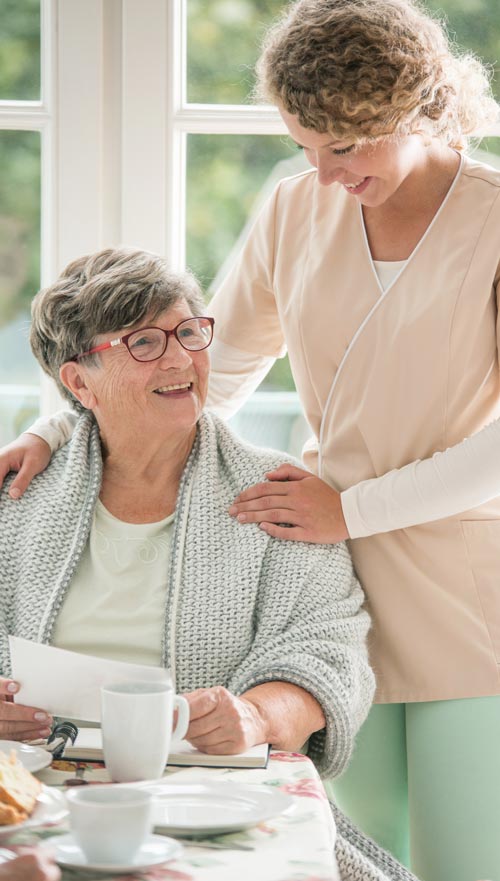 An elderly female resident holds a journal as she smiles with a younger female staff member.