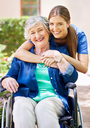 A nursing assistant hugs an elderly woman sitting in a wheelchair.