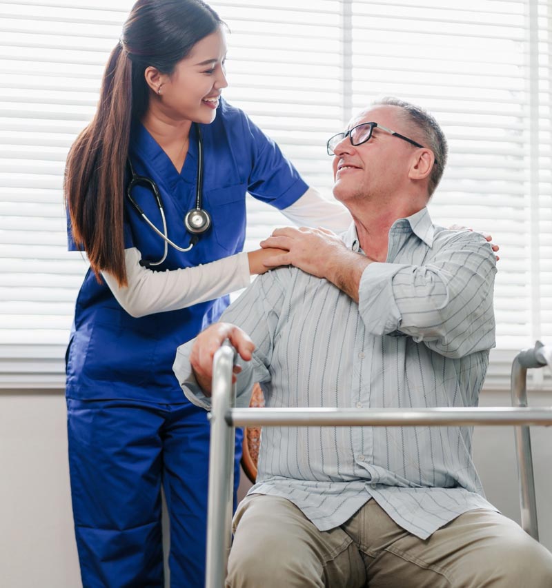 A young female therapy assistant and an elderly male resident smile.