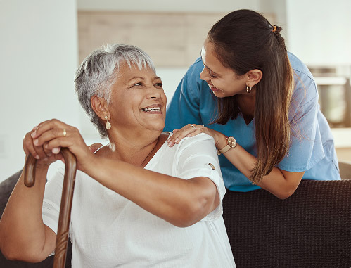 An elderly woman looks over her shoulder as a caregiver smiles at her.