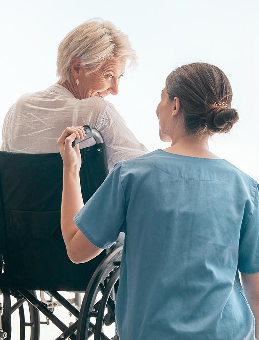 A group of seniors, three men and one woman, enjoy conversation around a dining table in a well-lit resident dining hall.